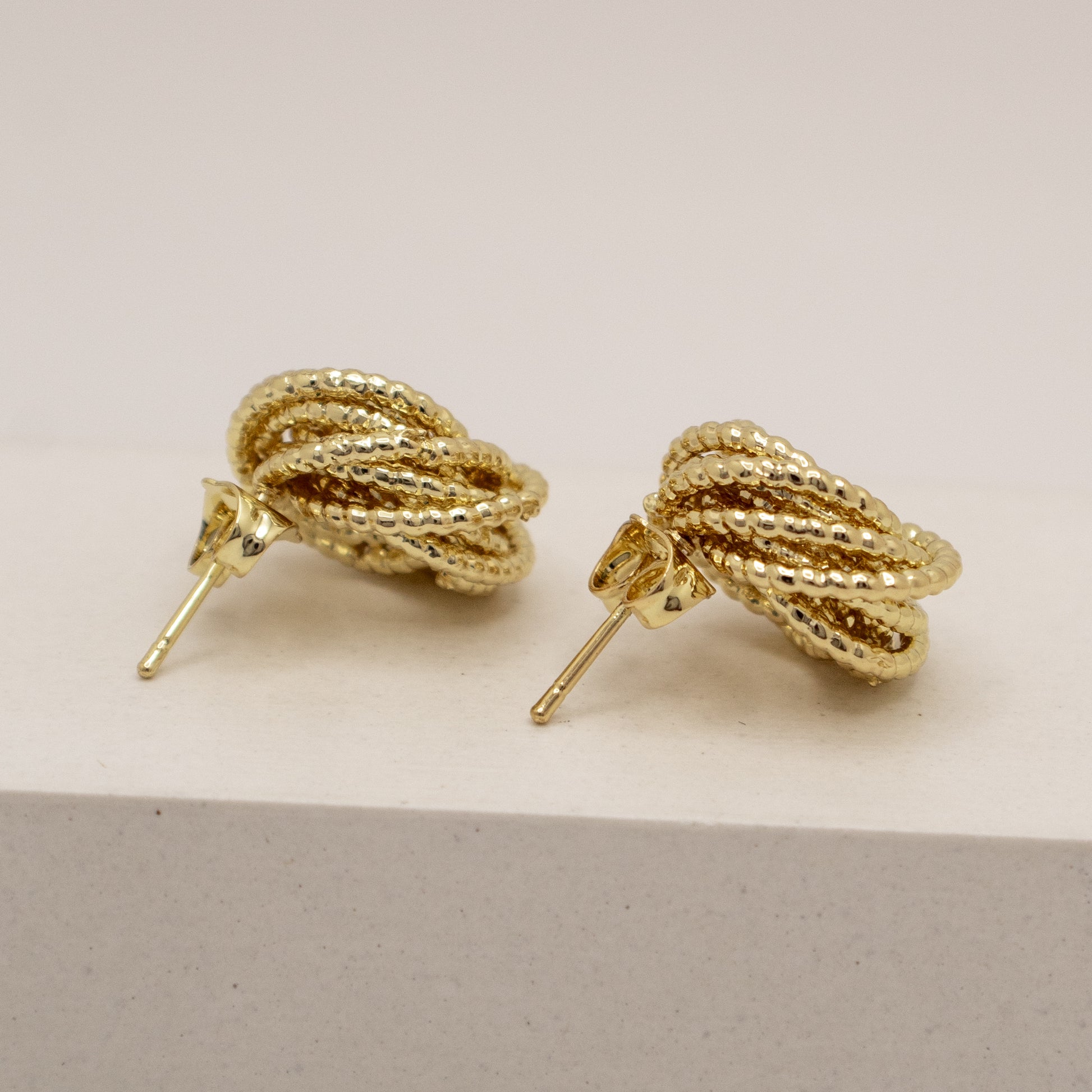 Gold rope-style earrings on a light beige background