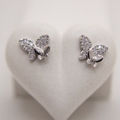 Butterfly-shaped silver earrings with clear stones on a heart-shaped white background