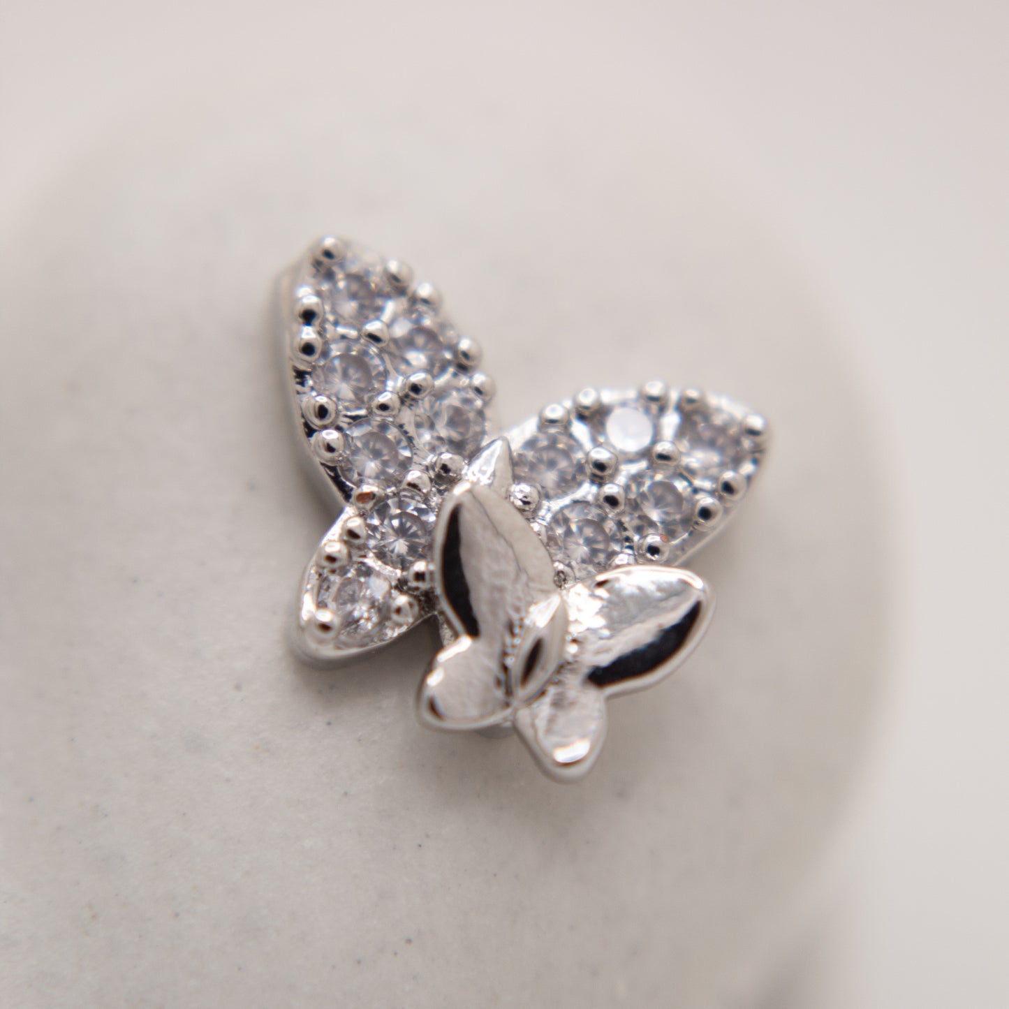 Silver butterfly-shaped earring with clear gemstones on a light gray background