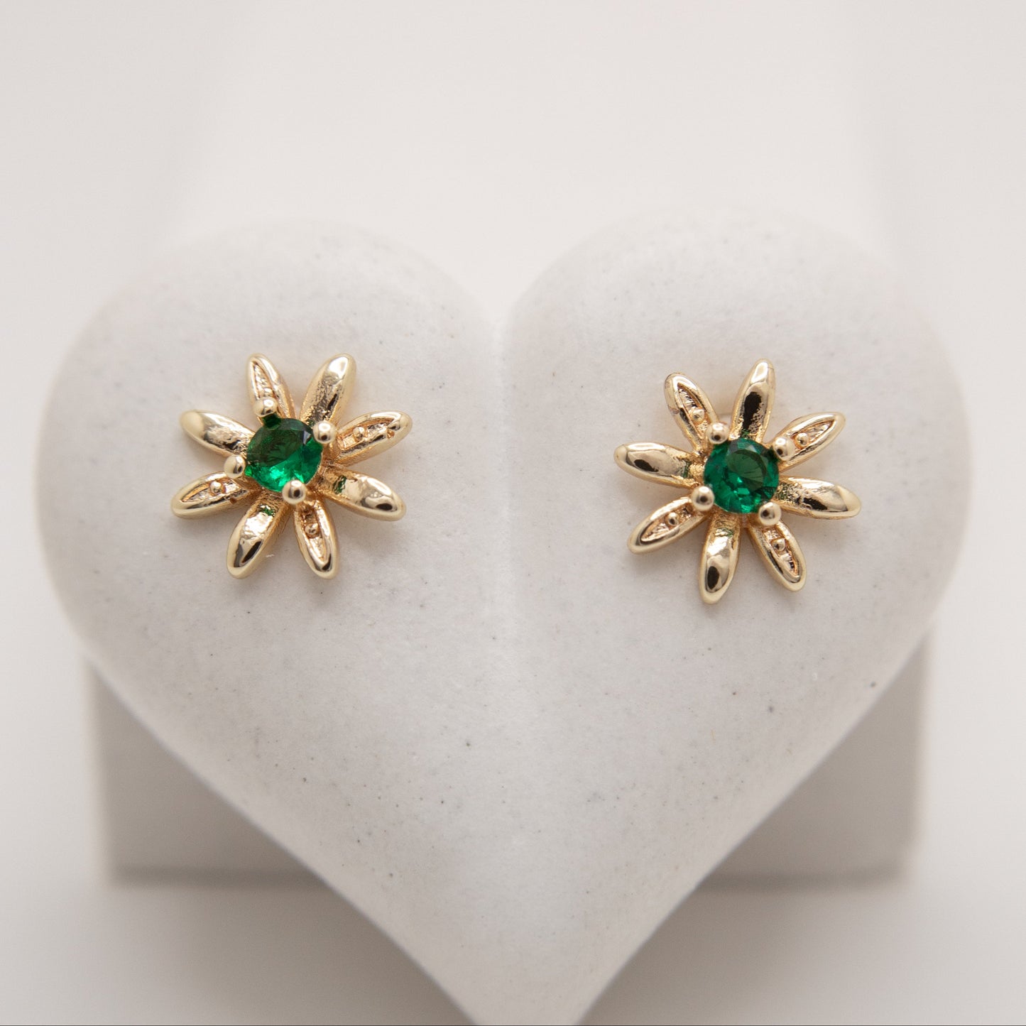 Gold earrings with green gemstones on a heart-shaped stand