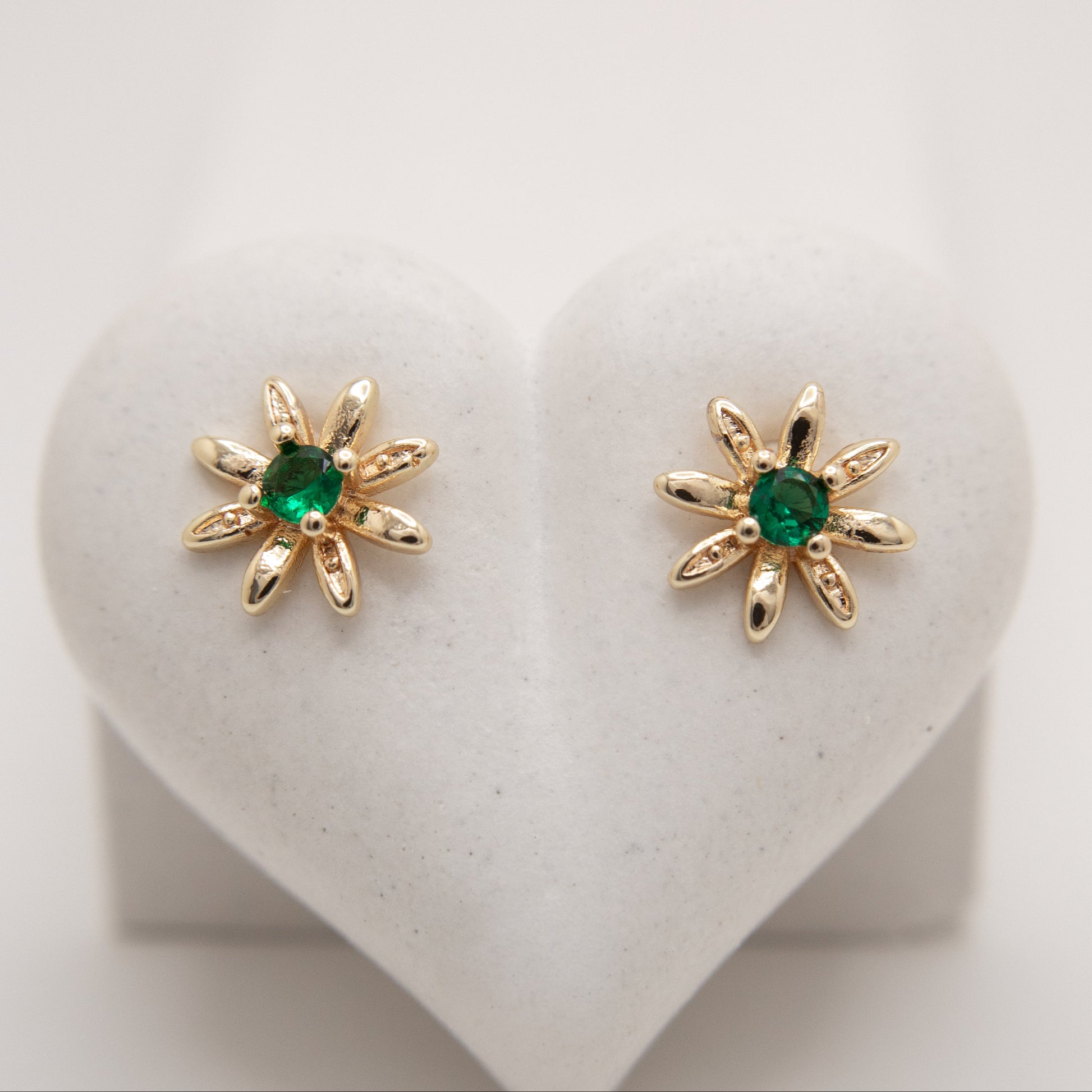 Gold earrings with green gemstones on a heart-shaped stand