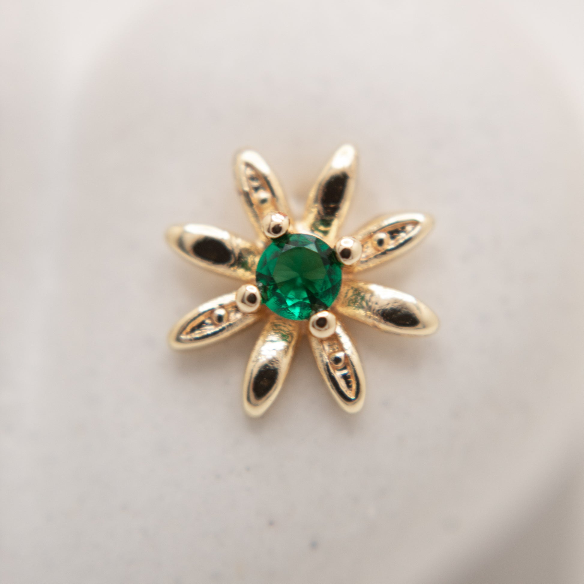 Gold flower-shaped pendant with a green gemstone on a light gray background