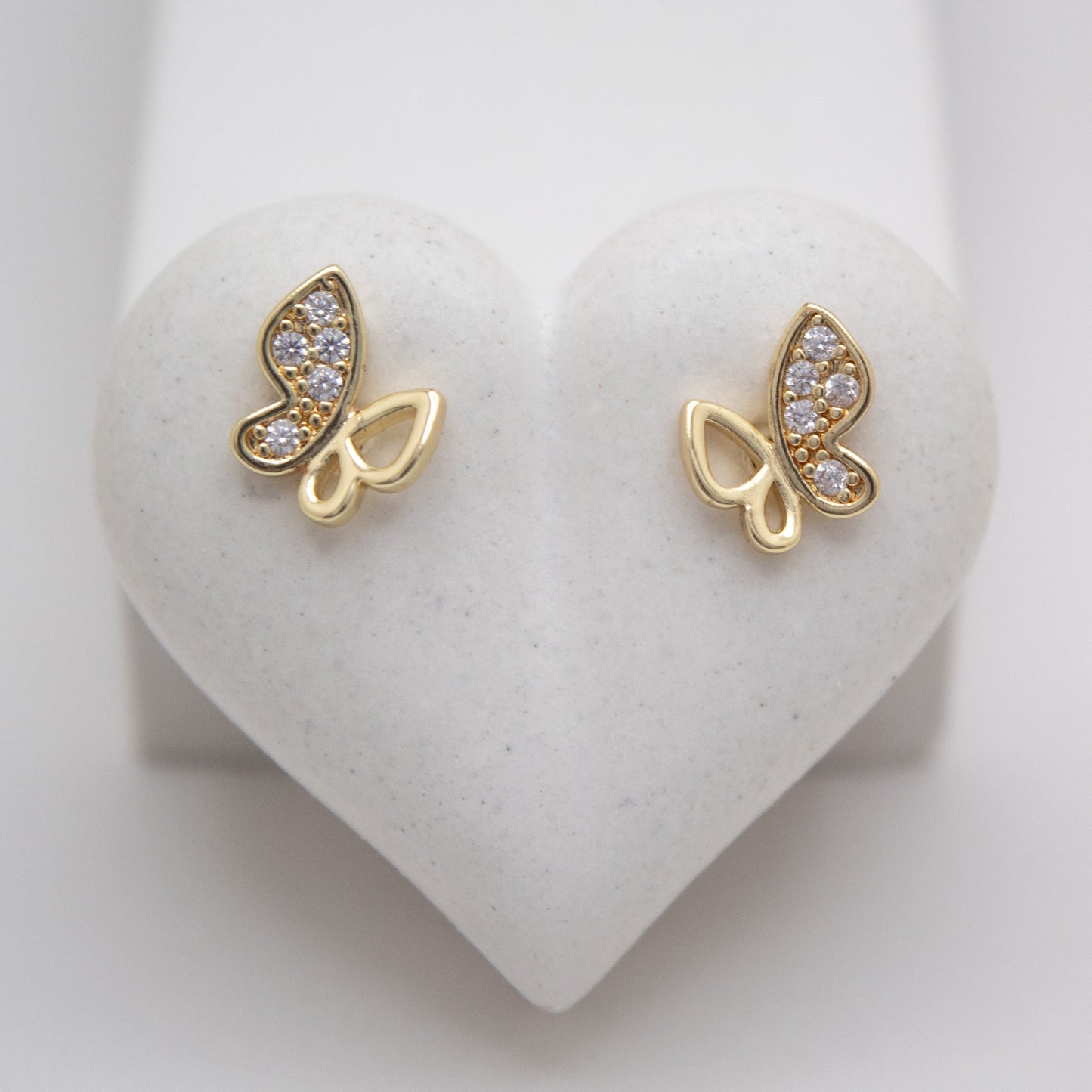 Gold butterfly earrings with gemstones on a heart-shaped white stand.