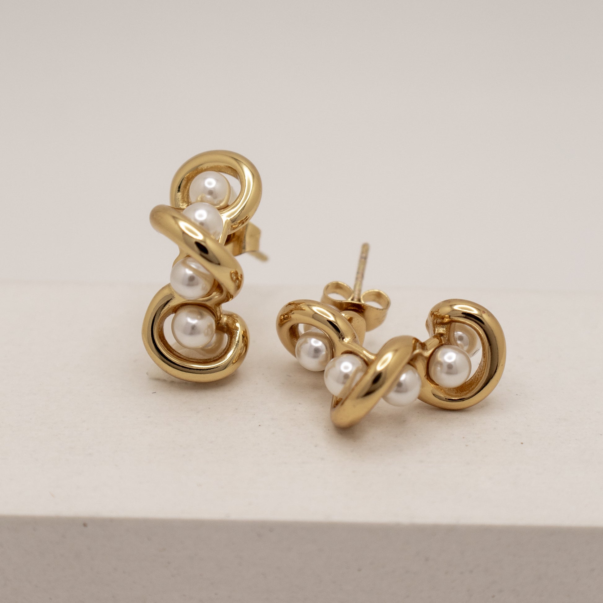 Gold earrings with pearls on a light beige background