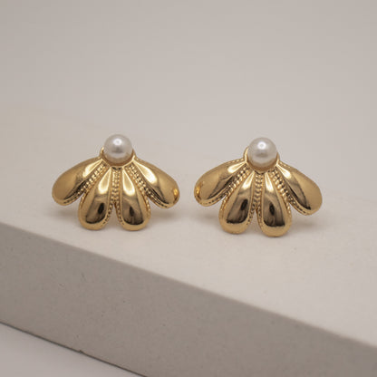 Pair of gold earrings with pearl centers on a neutral background