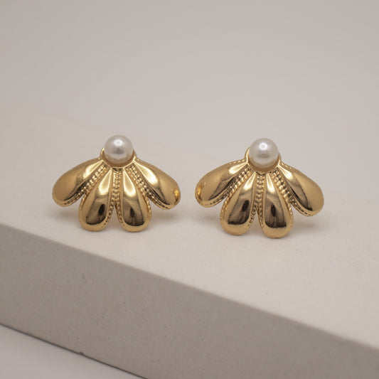Pair of gold earrings with pearl centers on a neutral background