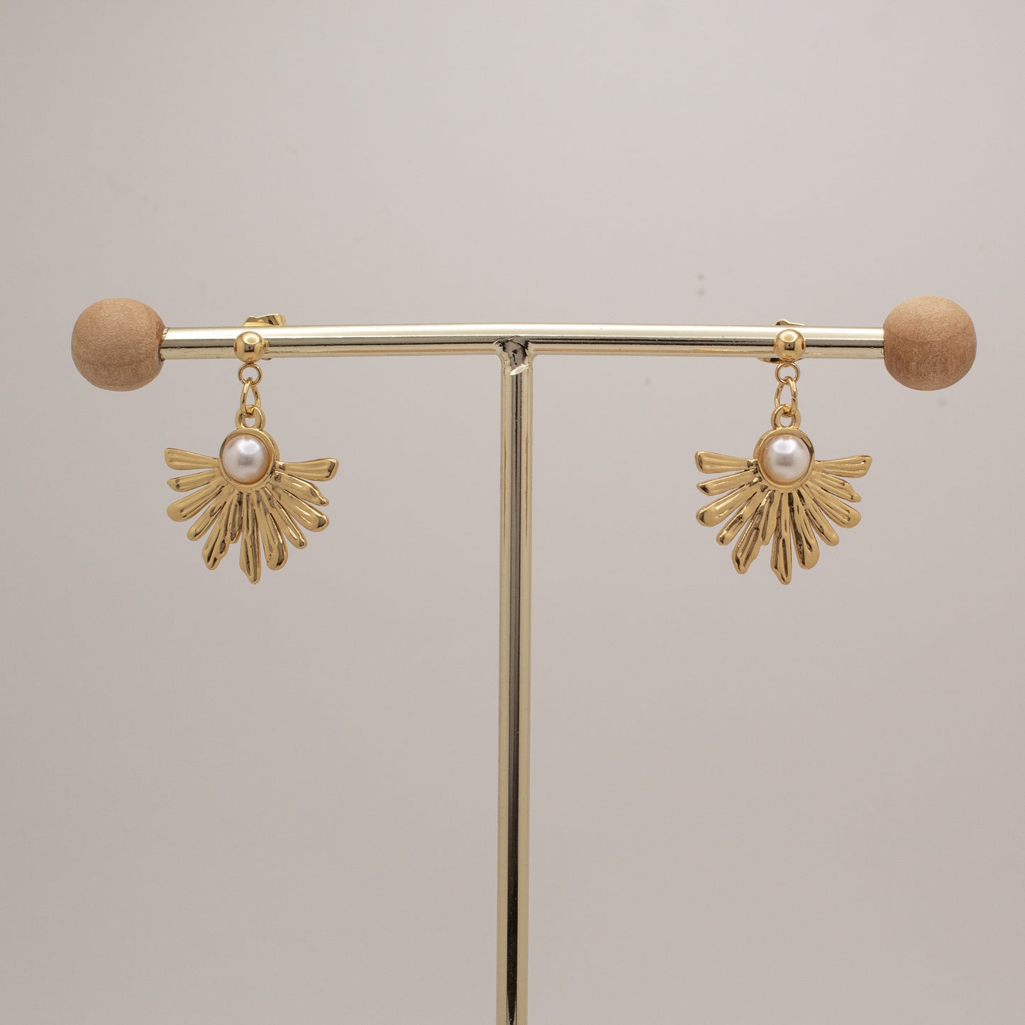Gold earrings with pearl drops on a gold stand against a beige background