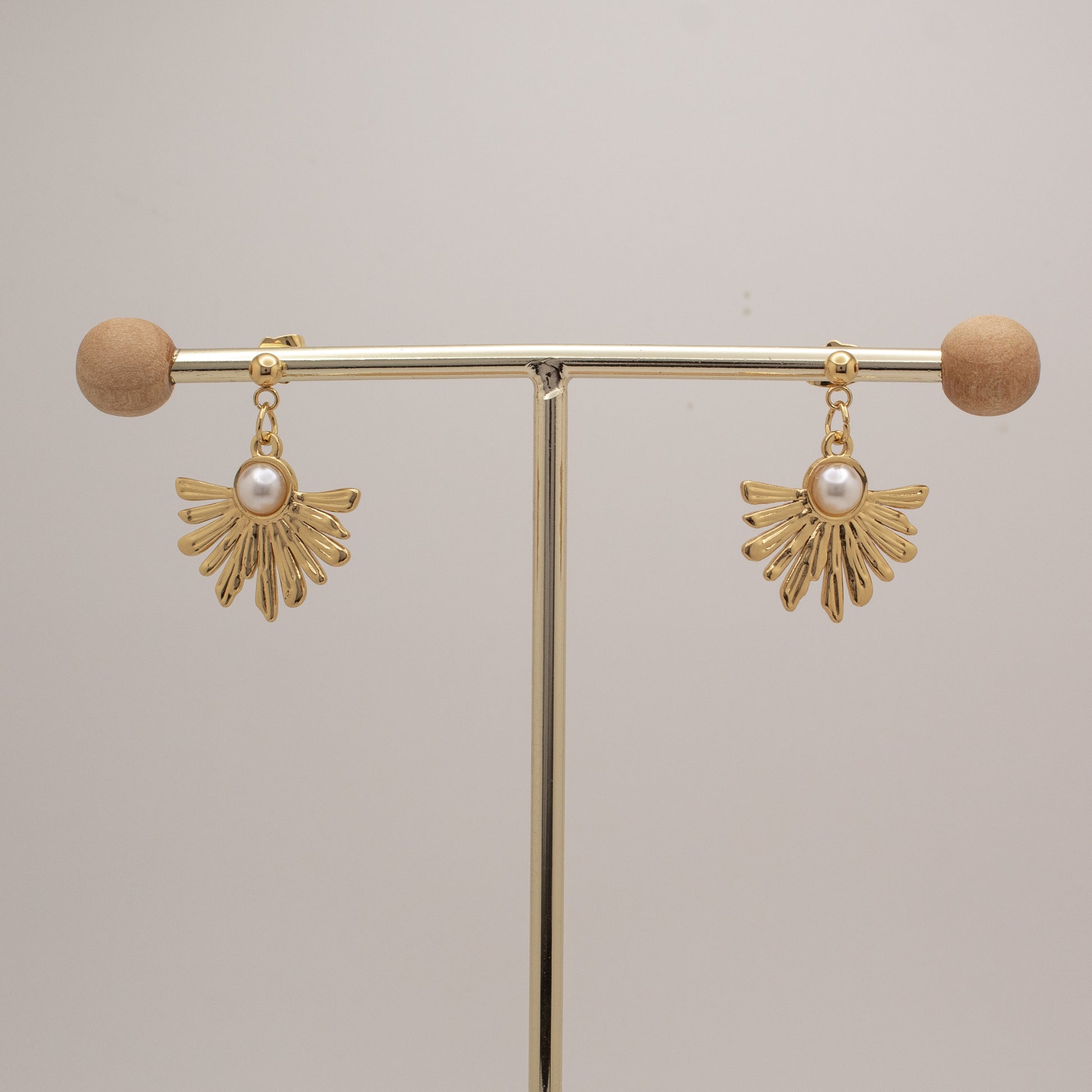 Gold earrings with pearl drops on a gold stand against a beige background