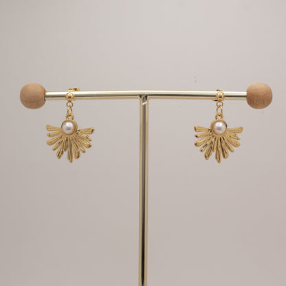 Gold earrings with pearl drops on a gold stand against a beige background