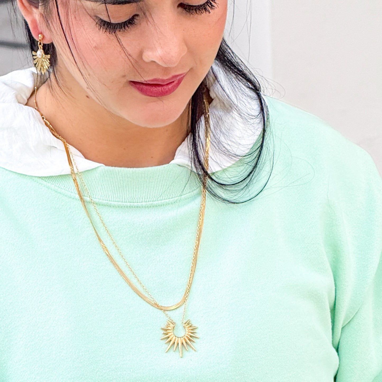Woman wearing a gold necklace with a sun design on a light green background