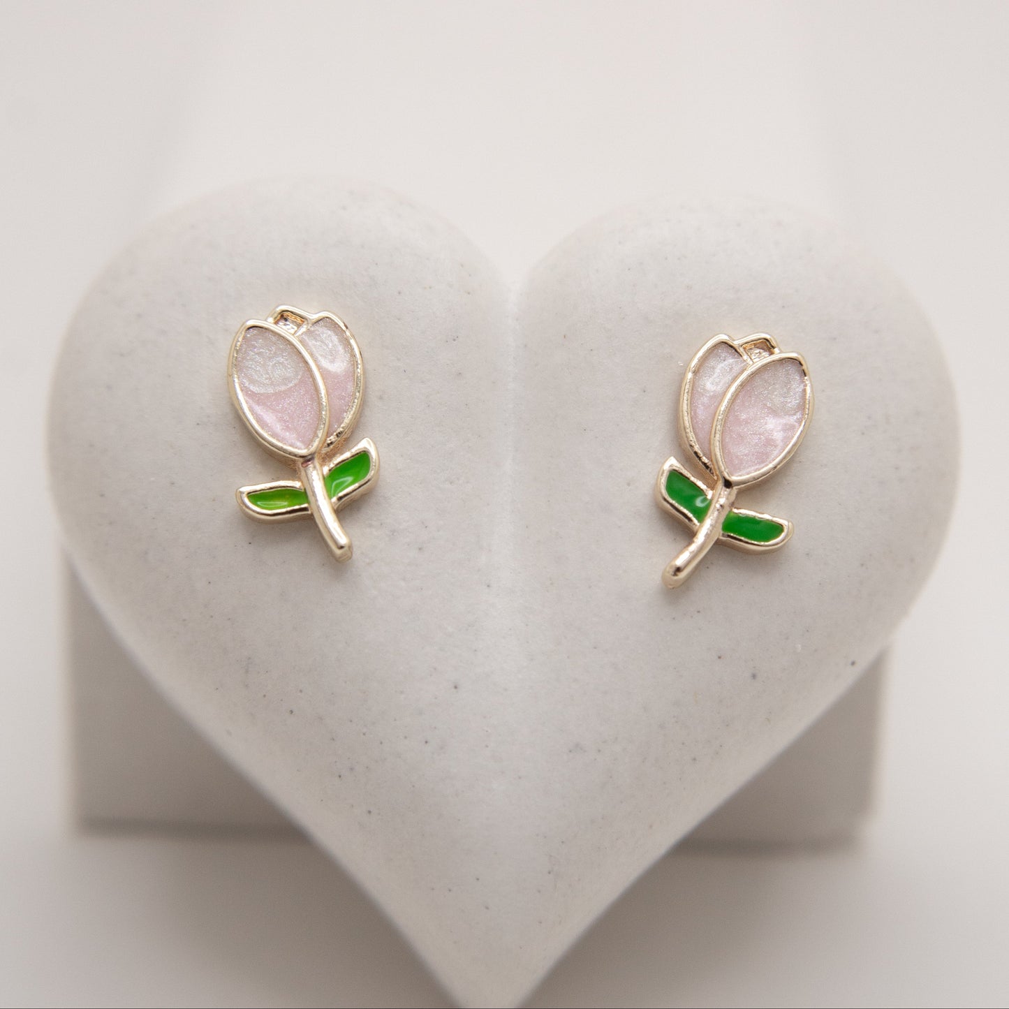 Pair of tulip-shaped earrings with pink centers and green accents on a heart-shaped stand.