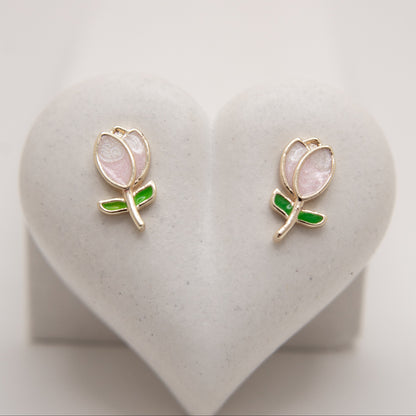 Pair of tulip-shaped earrings with pink centers and green accents on a heart-shaped stand.