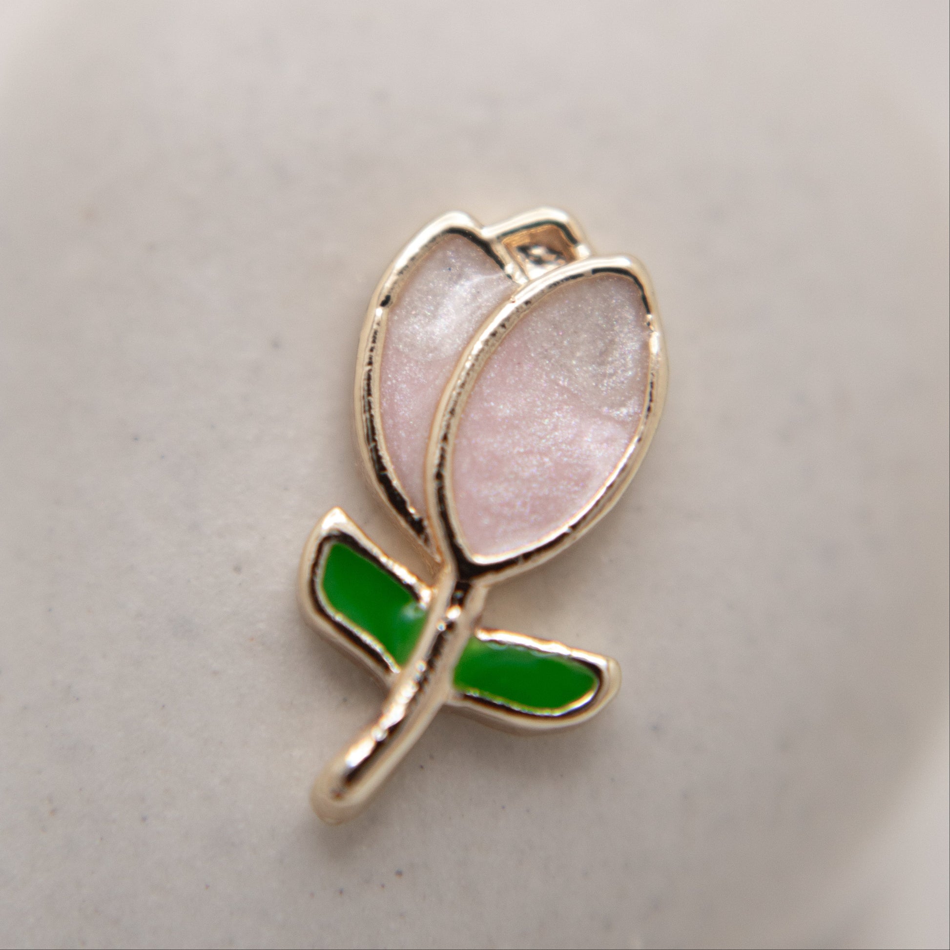 Tulip-shaped charm with pink center and green leaf on a light gray background