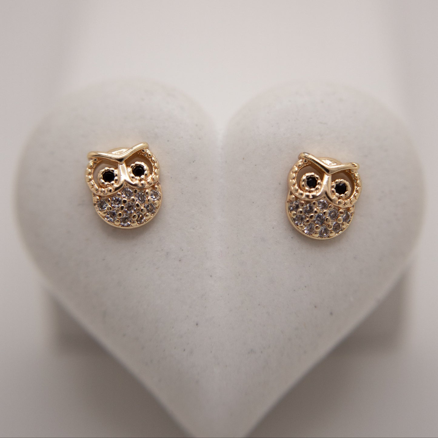 Gold owl-shaped earrings on a white heart-shaped stand