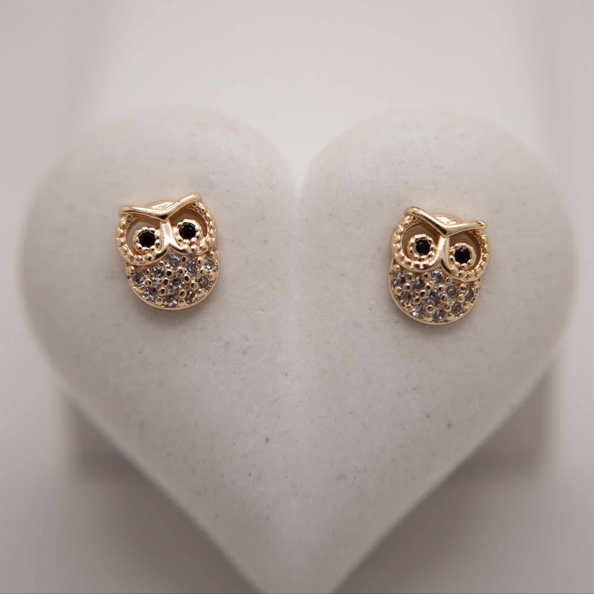 Gold owl-shaped earrings on a white heart-shaped stand