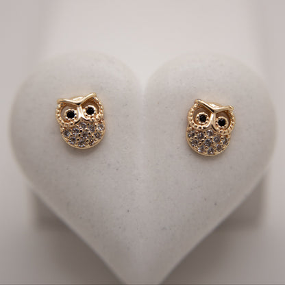 Gold owl-shaped earrings on a white heart-shaped stand