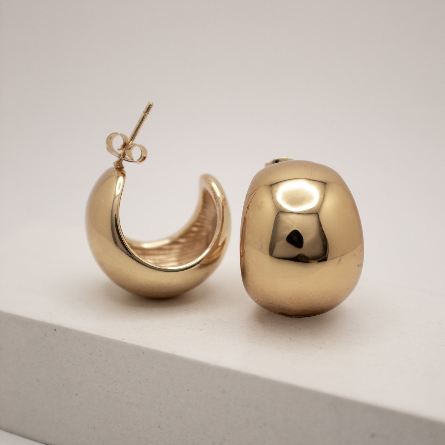 Gold hoop earrings on a light gray surface with a white background