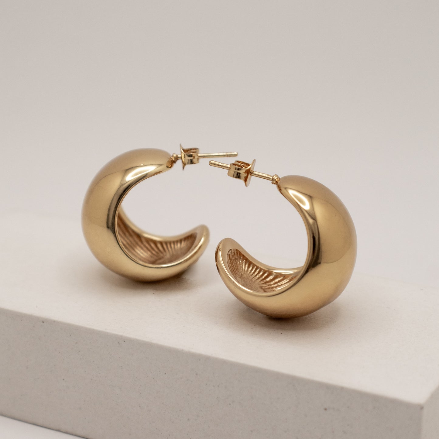 Gold hoop earrings on a light gray surface with a white background