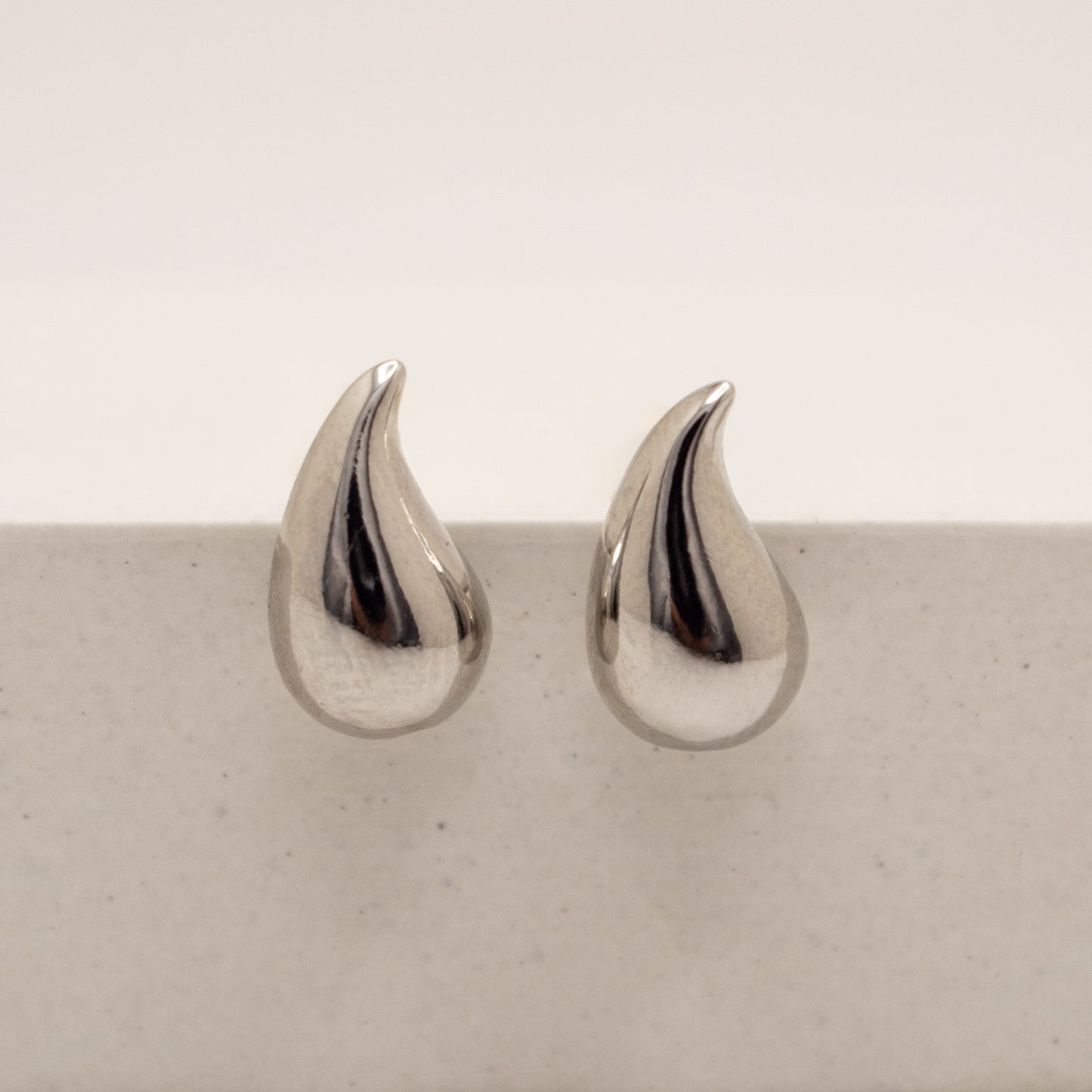Pair of silver teardrop-shaped earrings on a light gray surface.
