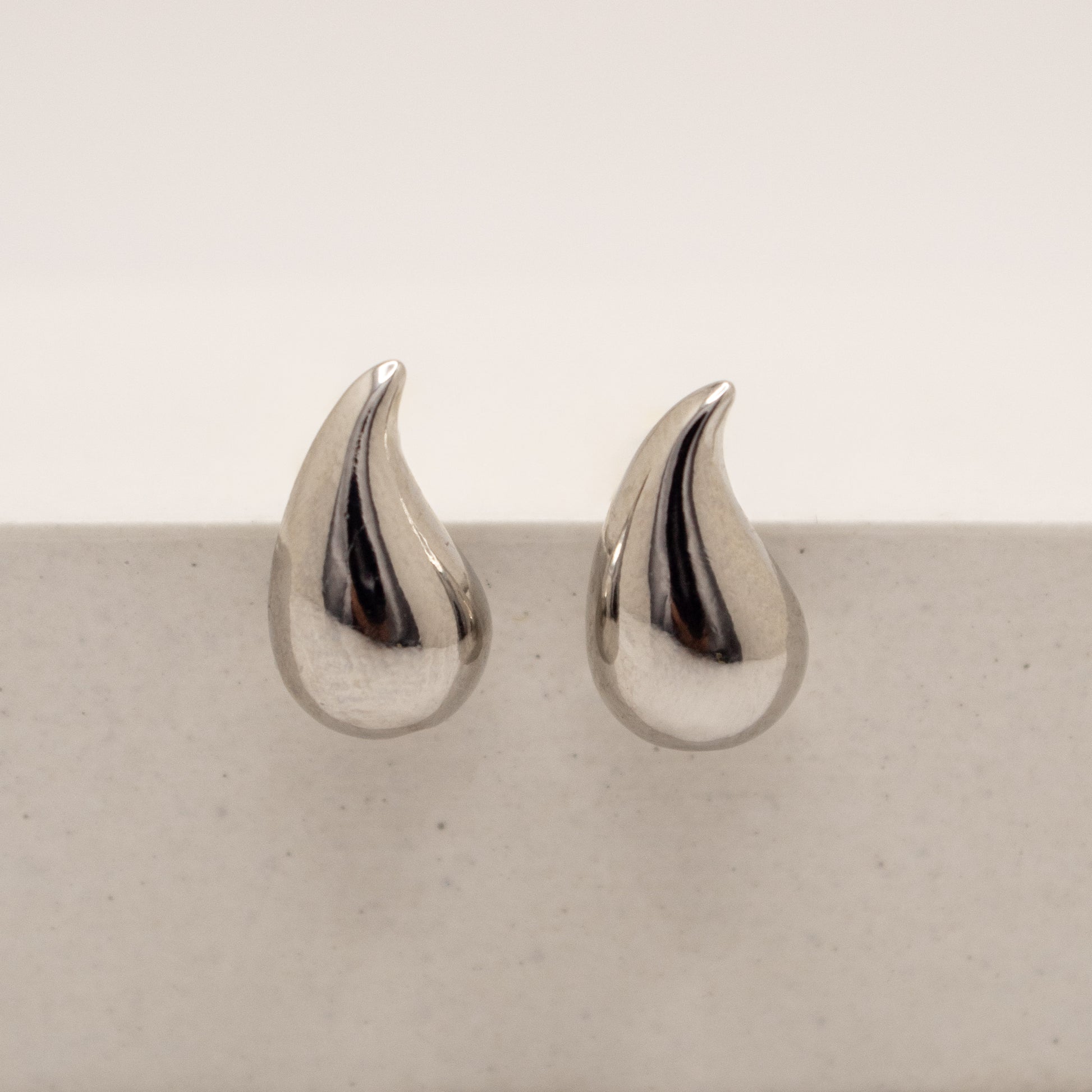 Pair of silver teardrop-shaped earrings on a light gray surface.