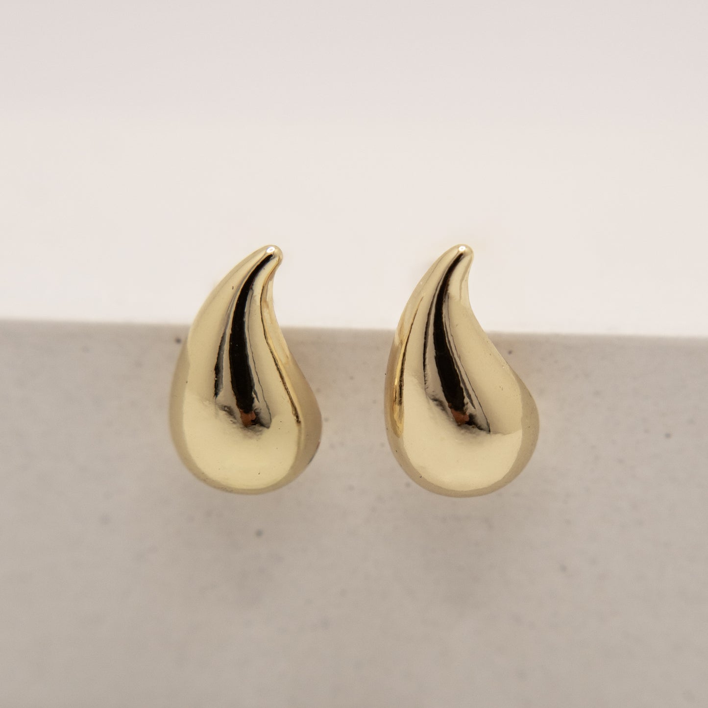 Gold teardrop-shaped earrings on a light gray background