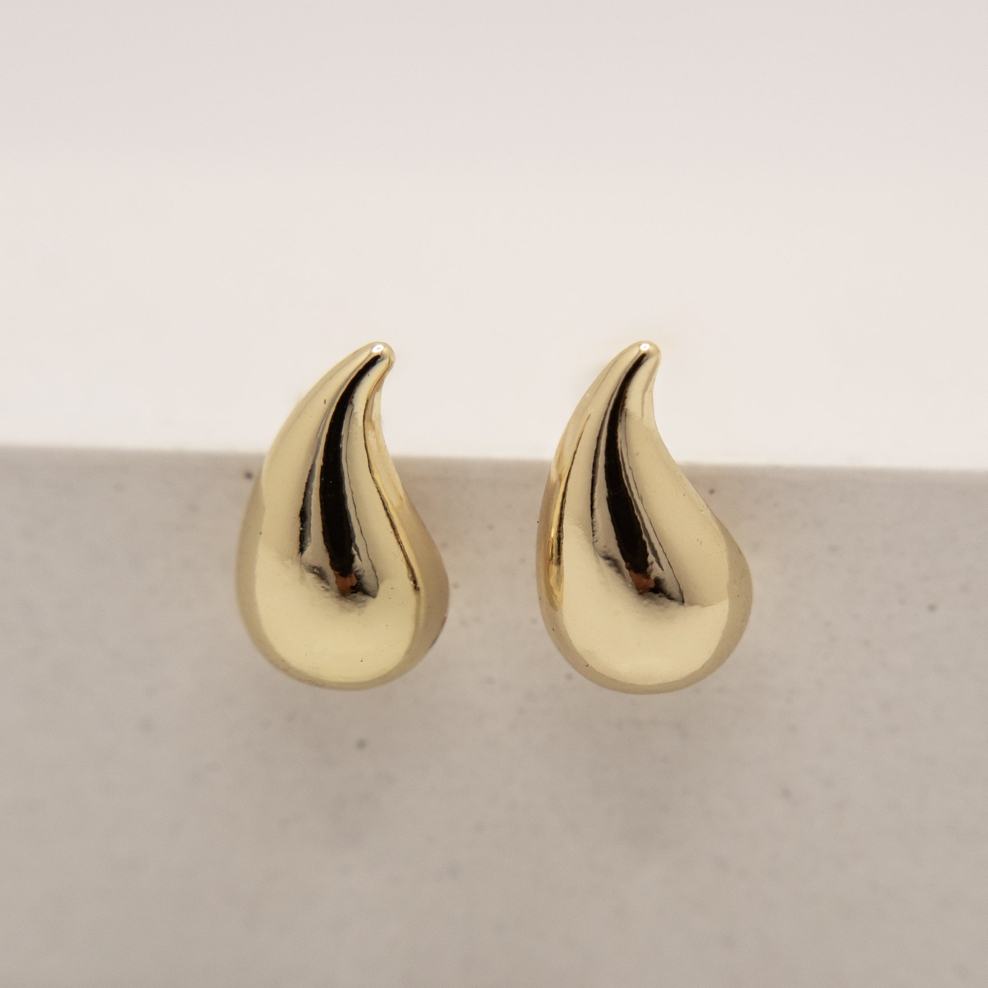 Gold teardrop-shaped earrings on a light gray background