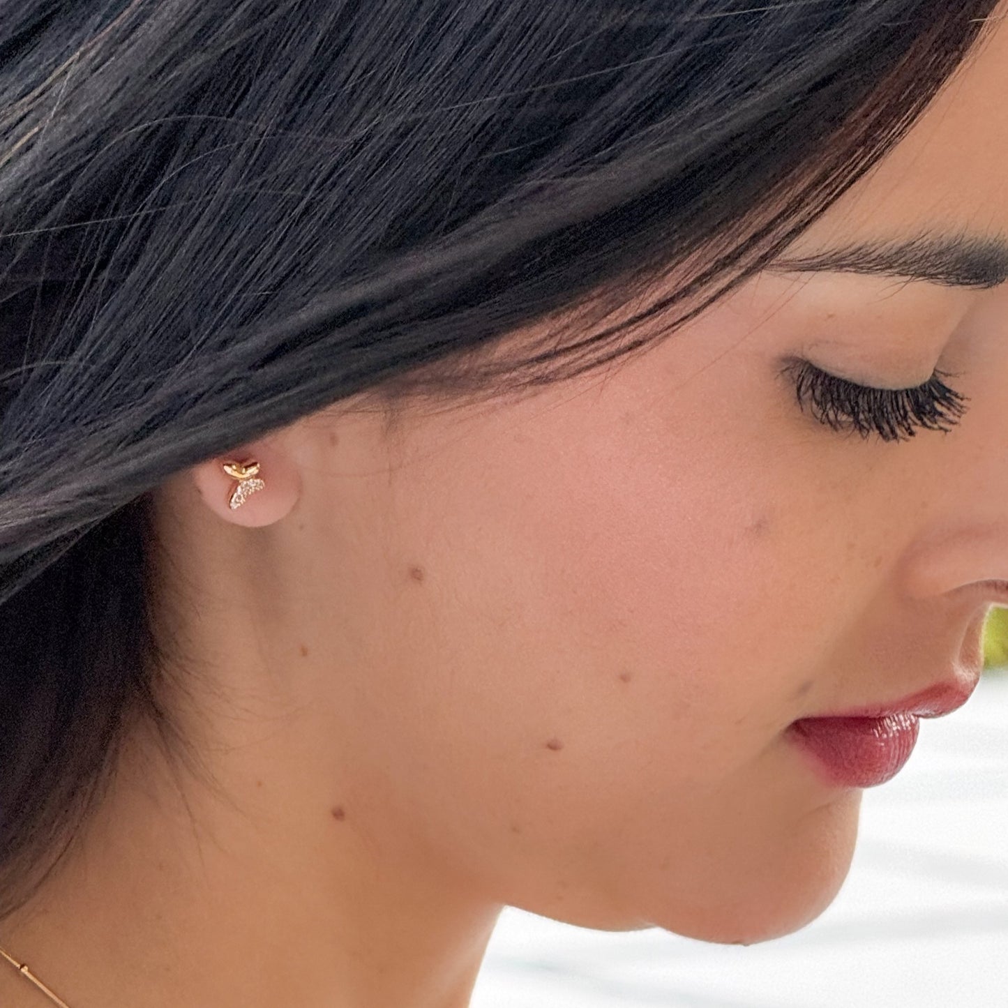 Close-up of a woman wearing a gold earring with a diamond on a blurred background