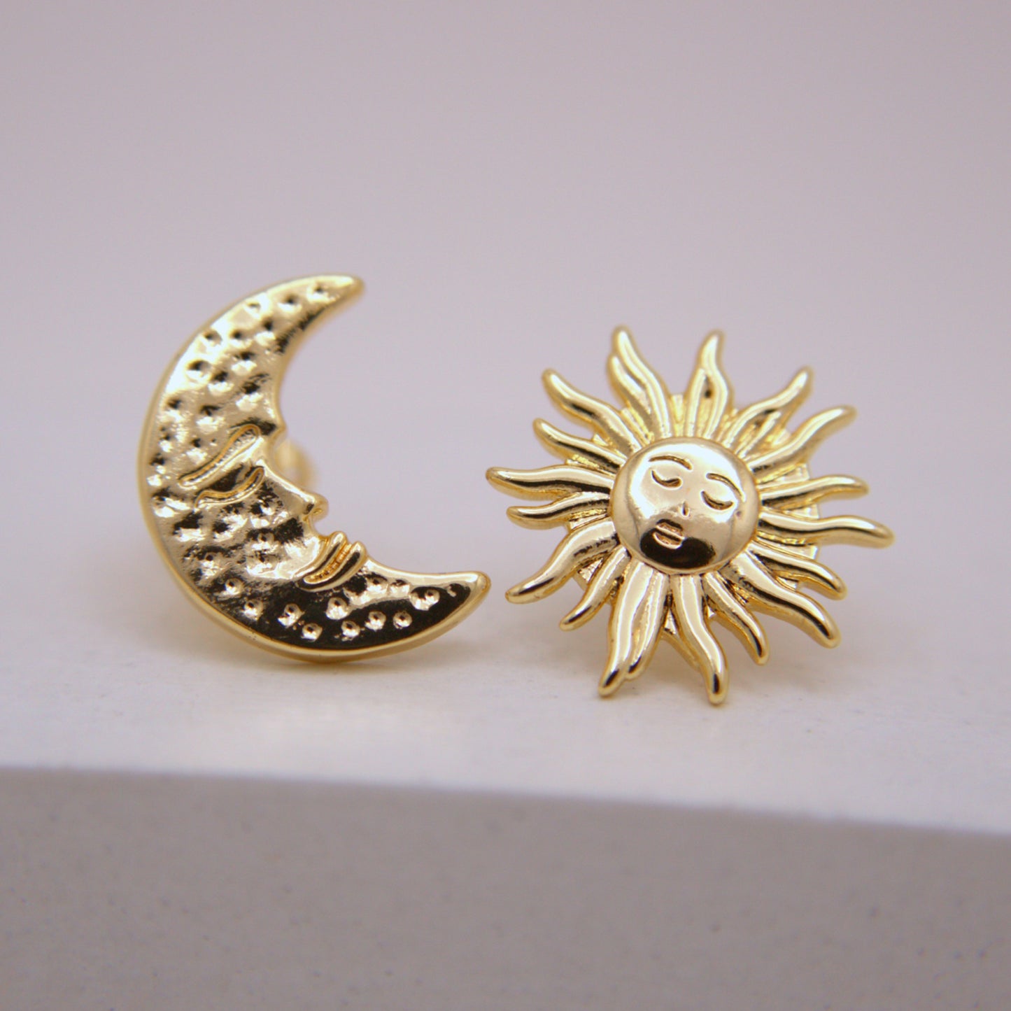 Gold moon and sun earrings on a light pink background