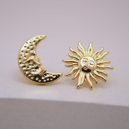 Gold moon and sun earrings on a light pink background