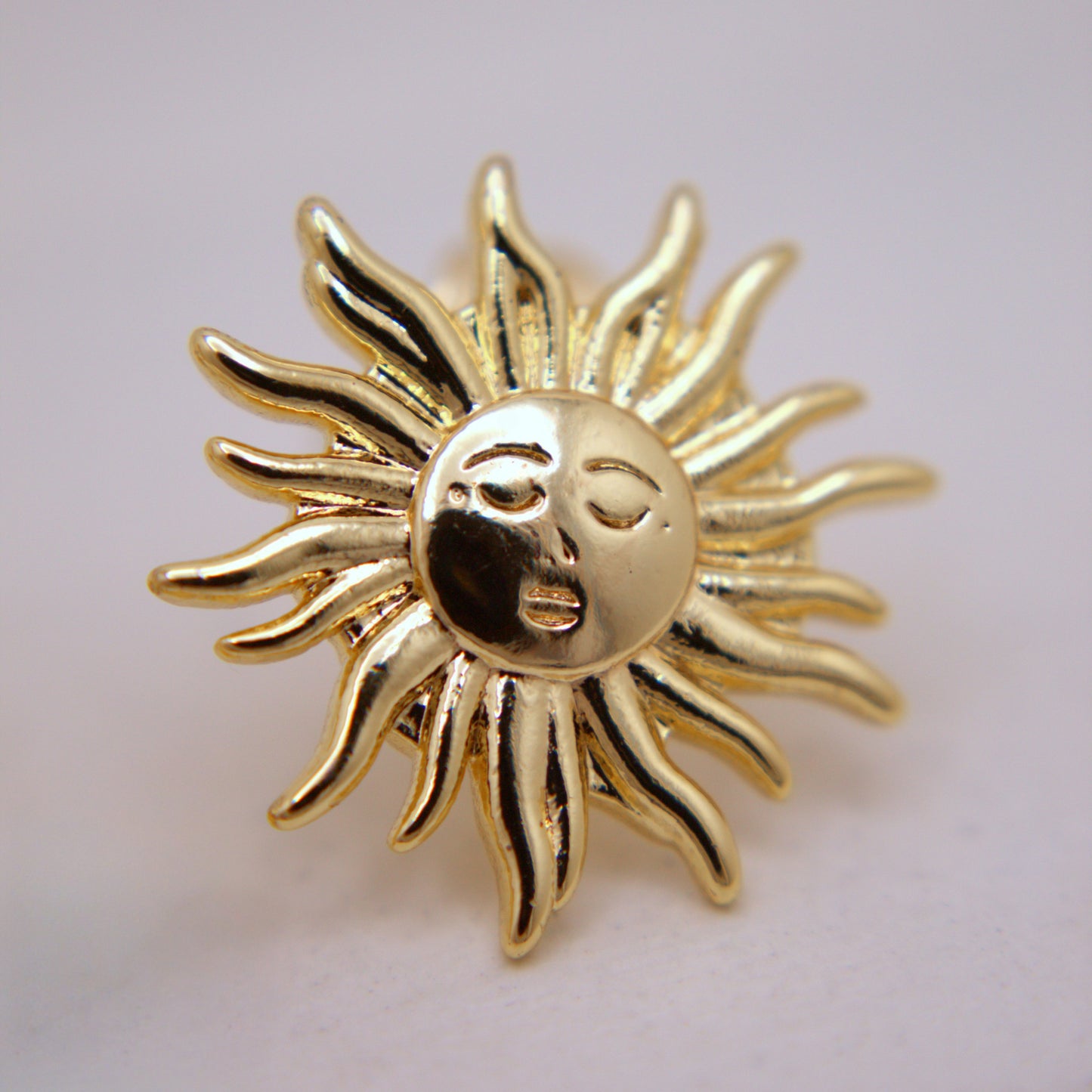 Gold sun-shaped brooch with face on a light gray background