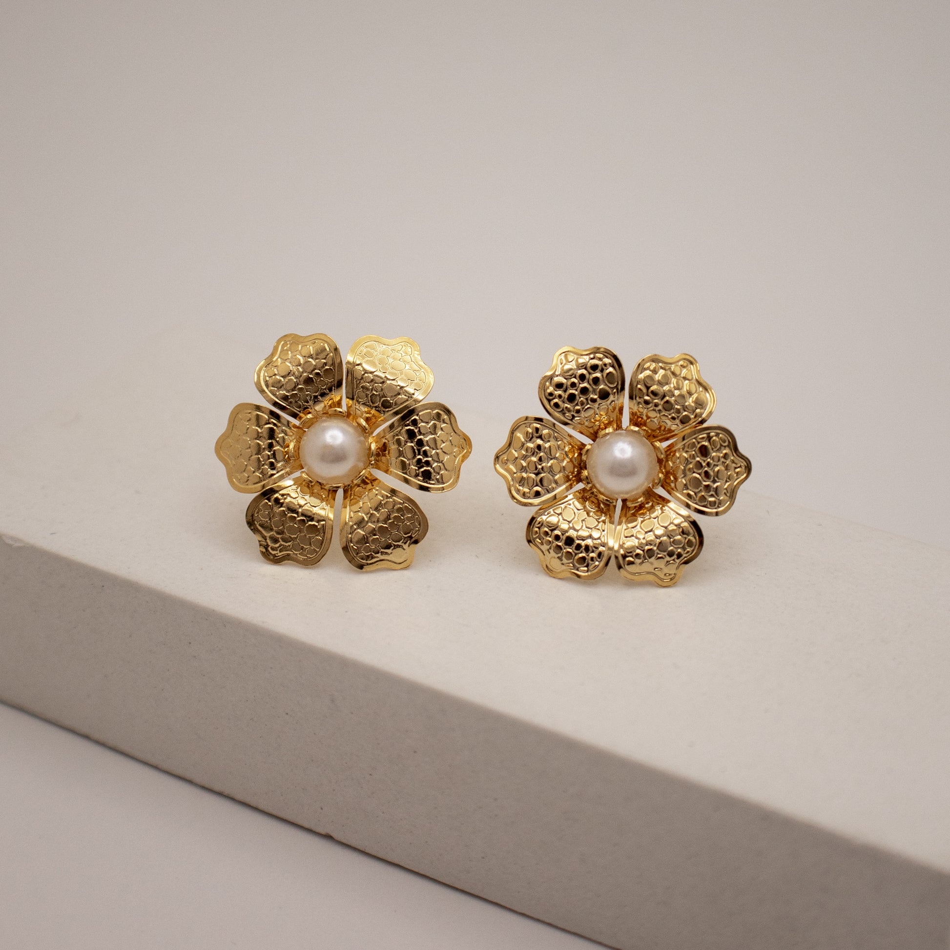 Gold flower-shaped earrings with pearl centers on a light gray background