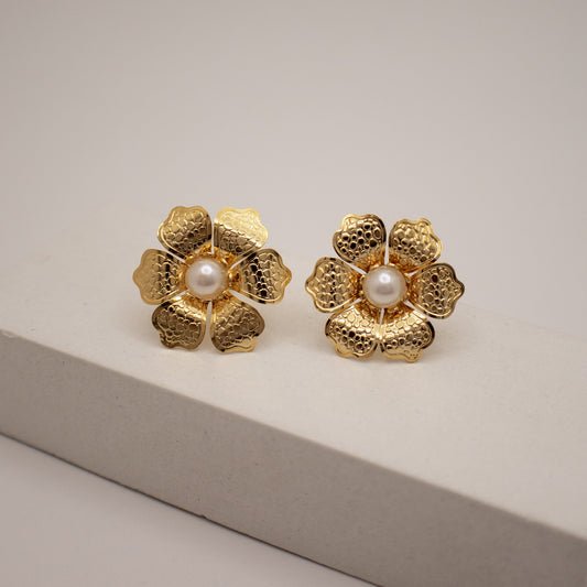 Gold flower-shaped earrings with pearl centers on a light gray background