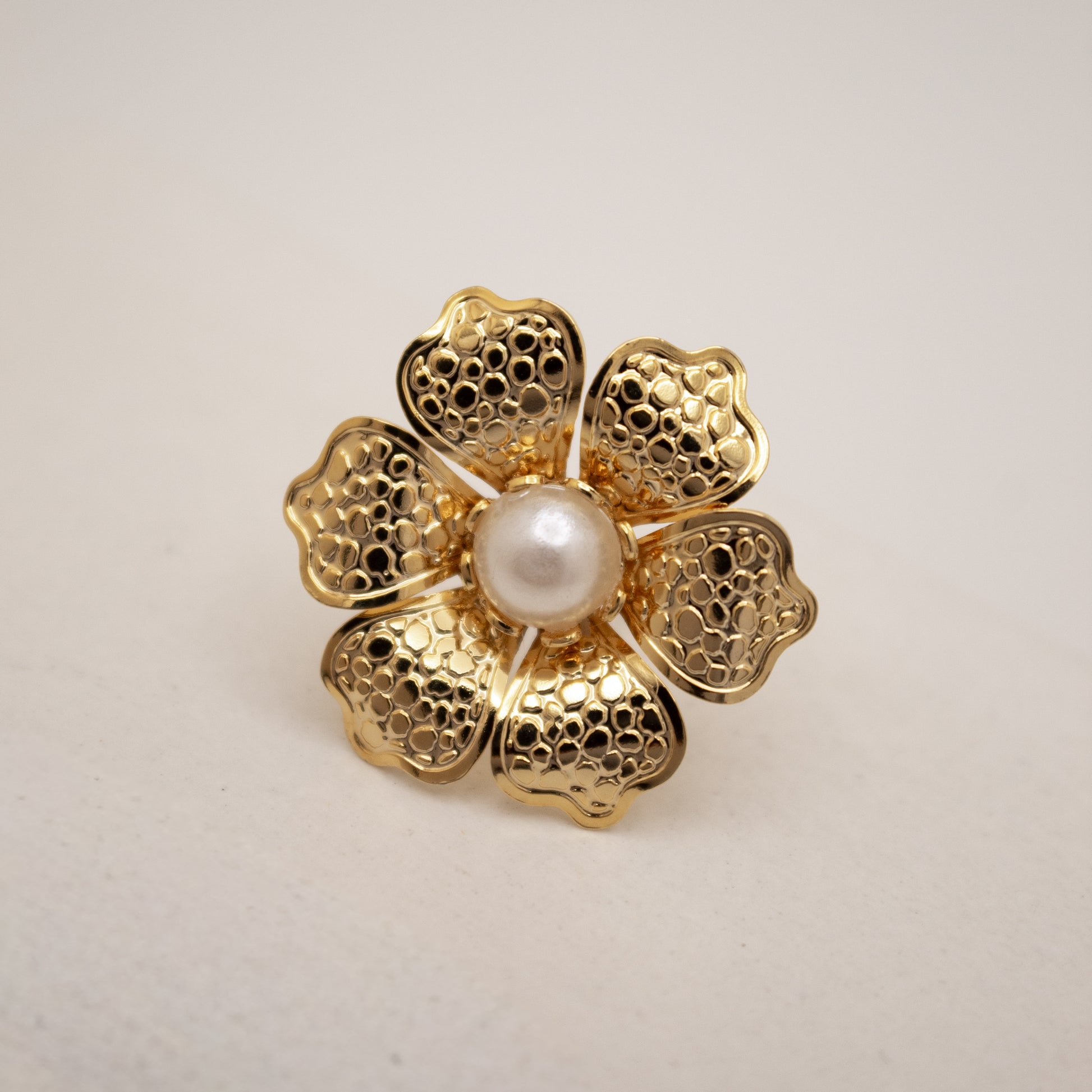 Gold flower-shaped stud with a pearl center on a light gray background