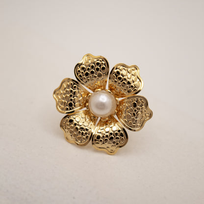 Gold flower-shaped stud with a pearl center on a light gray background
