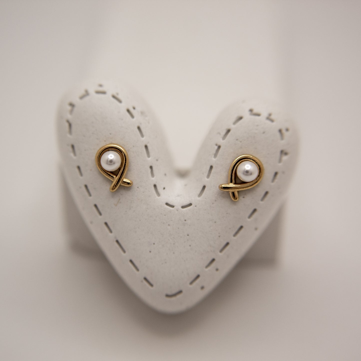 Pair of gold earrings with pearl-like stones on a heart-shaped white stand.