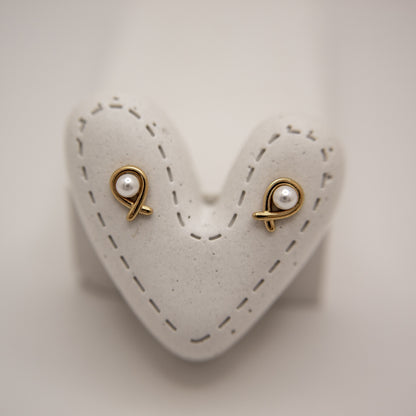 Pair of gold earrings with pearl-like stones on a heart-shaped white stand.