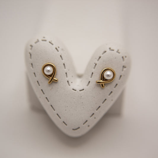 Pair of gold earrings with pearl-like stones on a heart-shaped white stand.