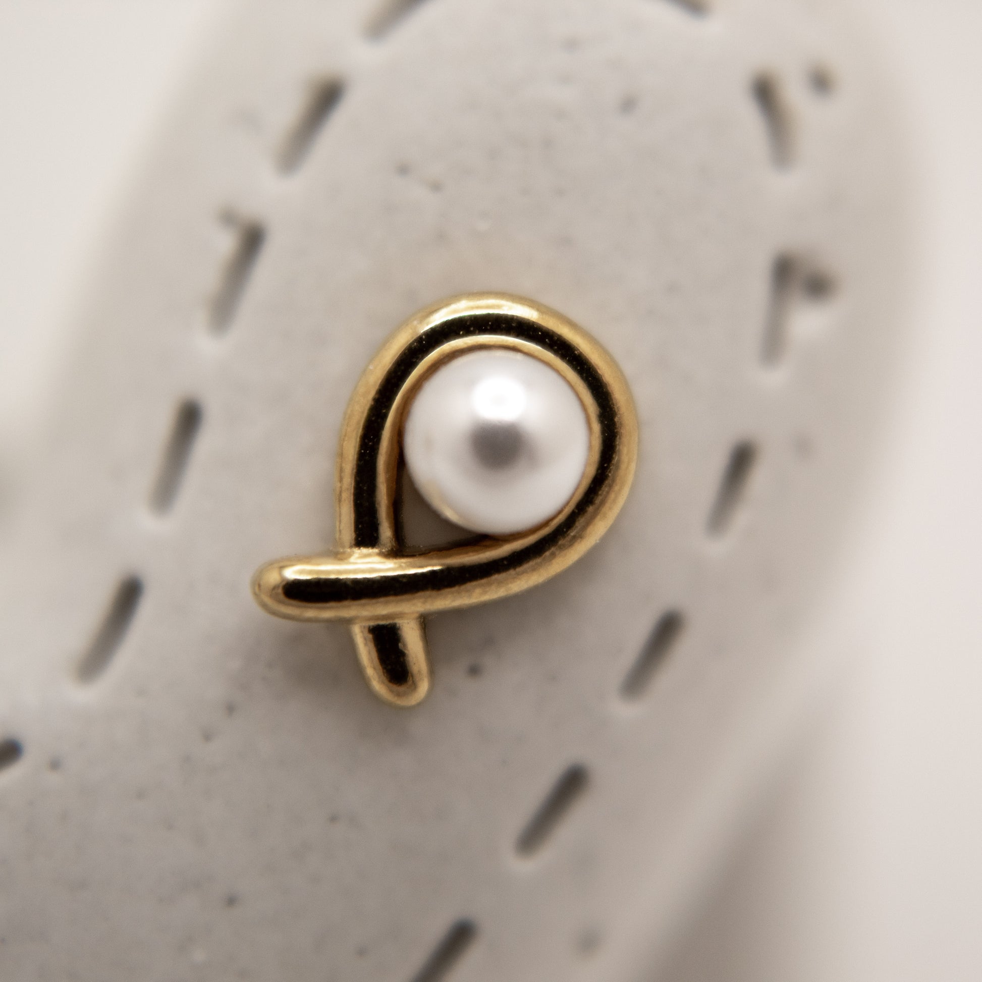 Gold brooch with a pearl on a textured beige background