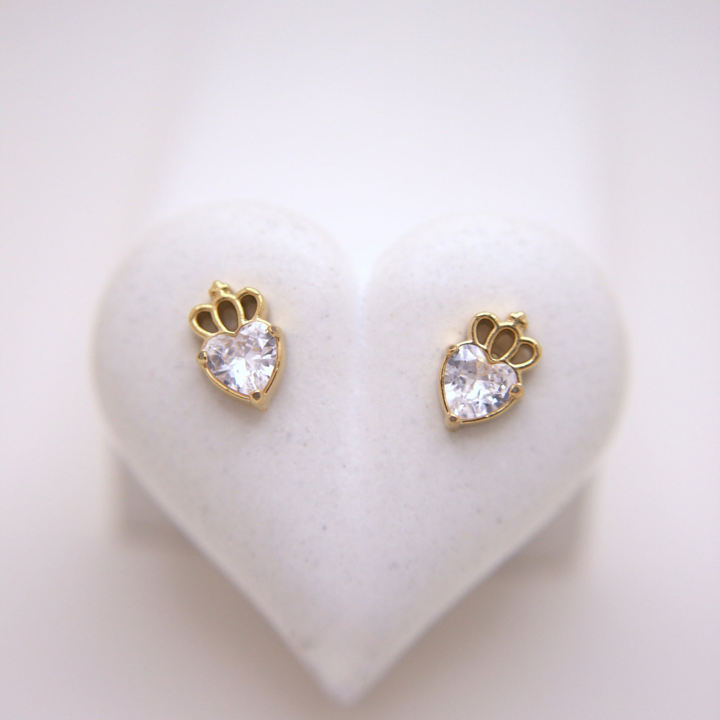 Heart-shaped earrings with clear gemstones on a heart-shaped stand.