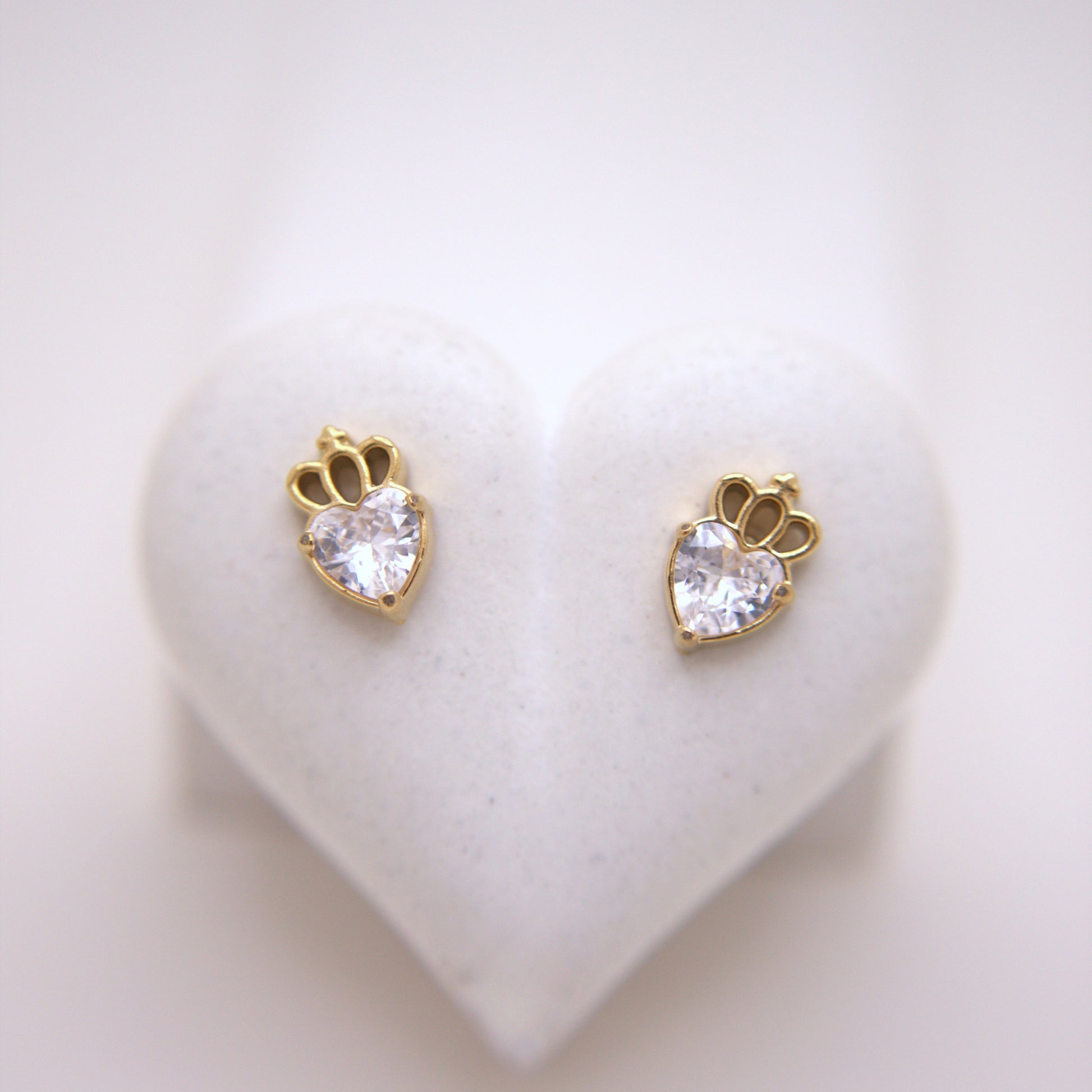 Heart-shaped earrings with clear gemstones on a heart-shaped stand.