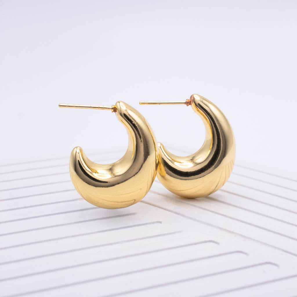A pair of gold crescent-shaped hoop earrings with a textured, ribbed finish and post-back closures, displayed on a white ribbed surface against a light gray background.