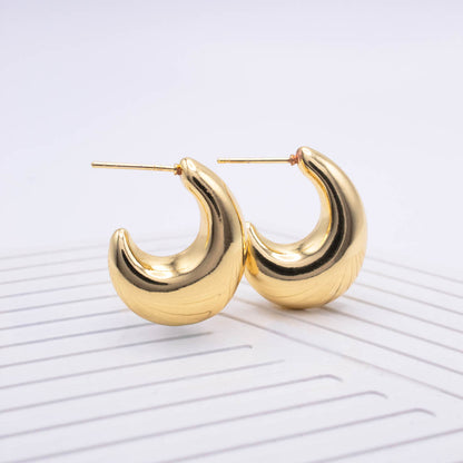 A pair of gold crescent-shaped hoop earrings with a textured, ribbed finish and post-back closures, displayed on a white ribbed surface against a light gray background.