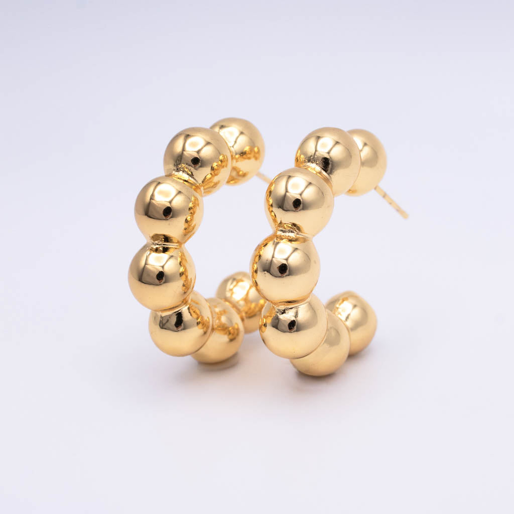 A pair of gold hoop earrings made of polished, glossy spherical beads, displayed on a clean white background.