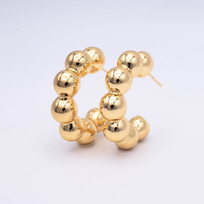 A pair of gold hoop earrings made of polished, glossy spherical beads, displayed on a clean white background.