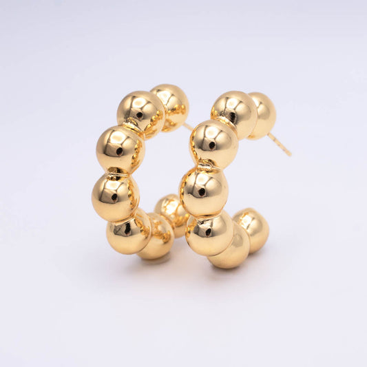 A pair of gold hoop earrings made of polished, glossy spherical beads, displayed on a clean white background.