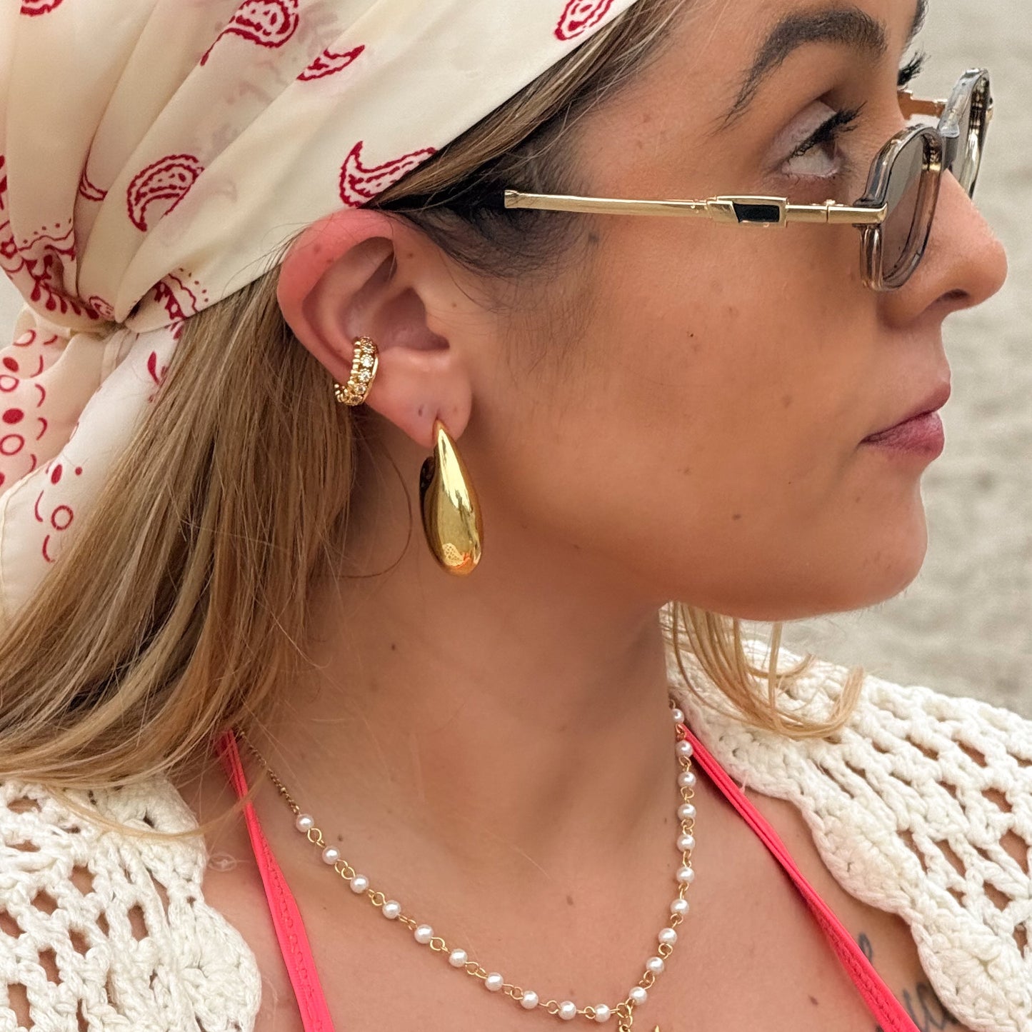 Woman wearing a pink bikini top, gold earrings, and a white headscarf with red patterns.