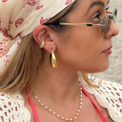 Woman wearing a pink bikini top, gold earrings, and a white headscarf with red patterns.