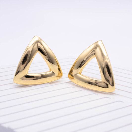 A pair of polished gold triangular stud earrings with a thick, open triangular frame design, displayed on a white textured surface.