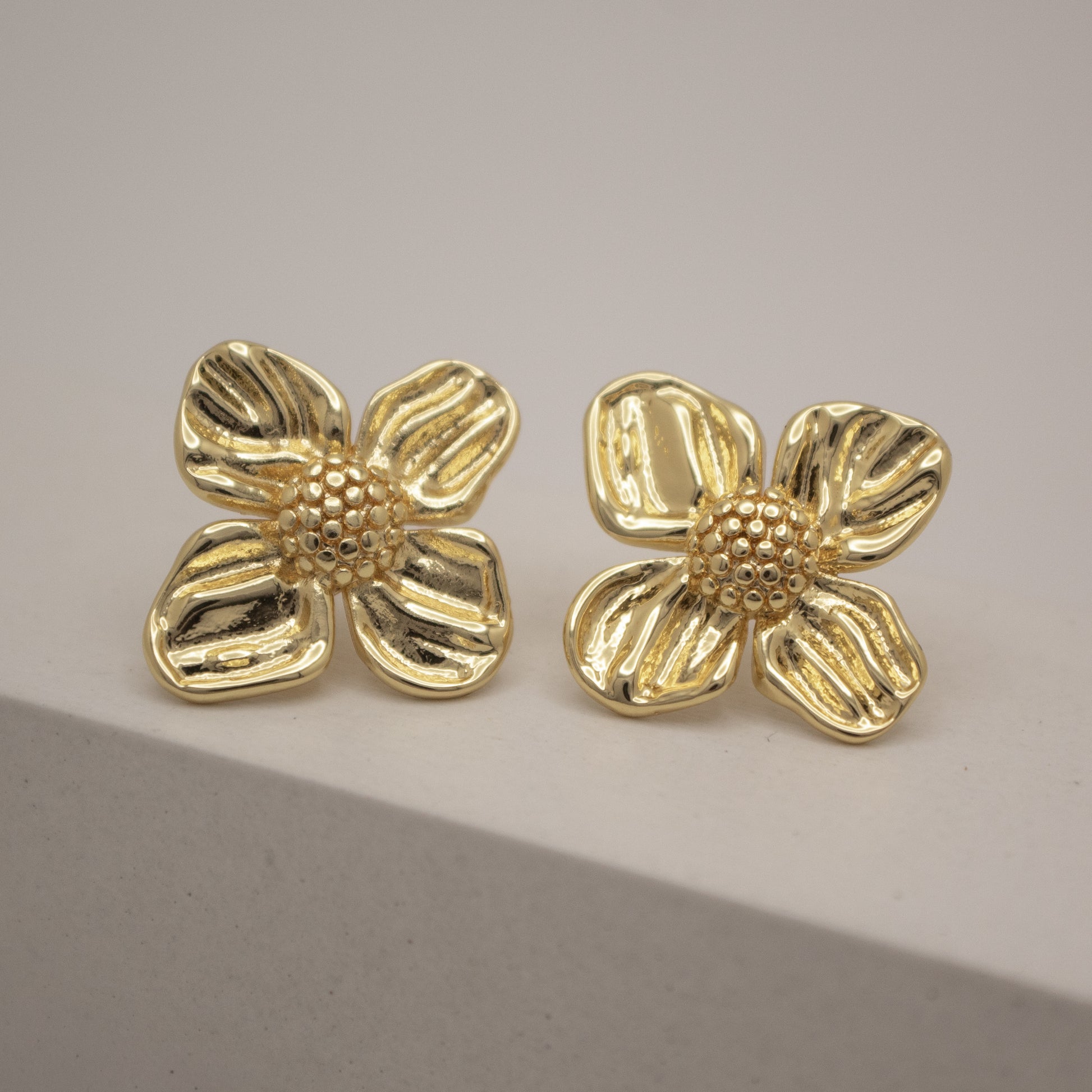 Pair of gold flower-shaped earrings on a neutral background