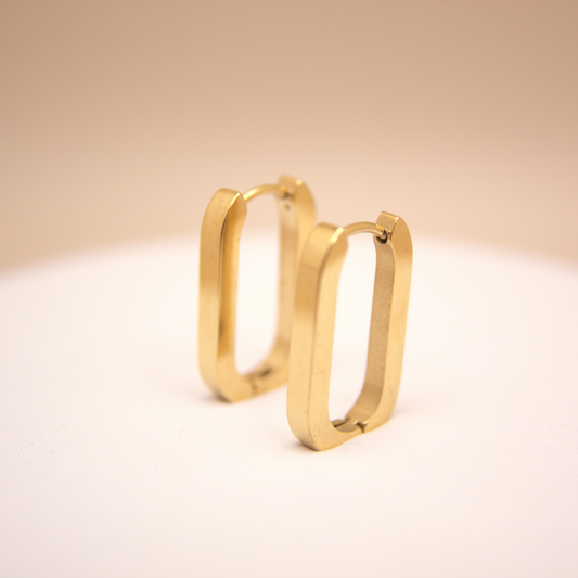 Gold hoop earrings on a white platform with a beige background